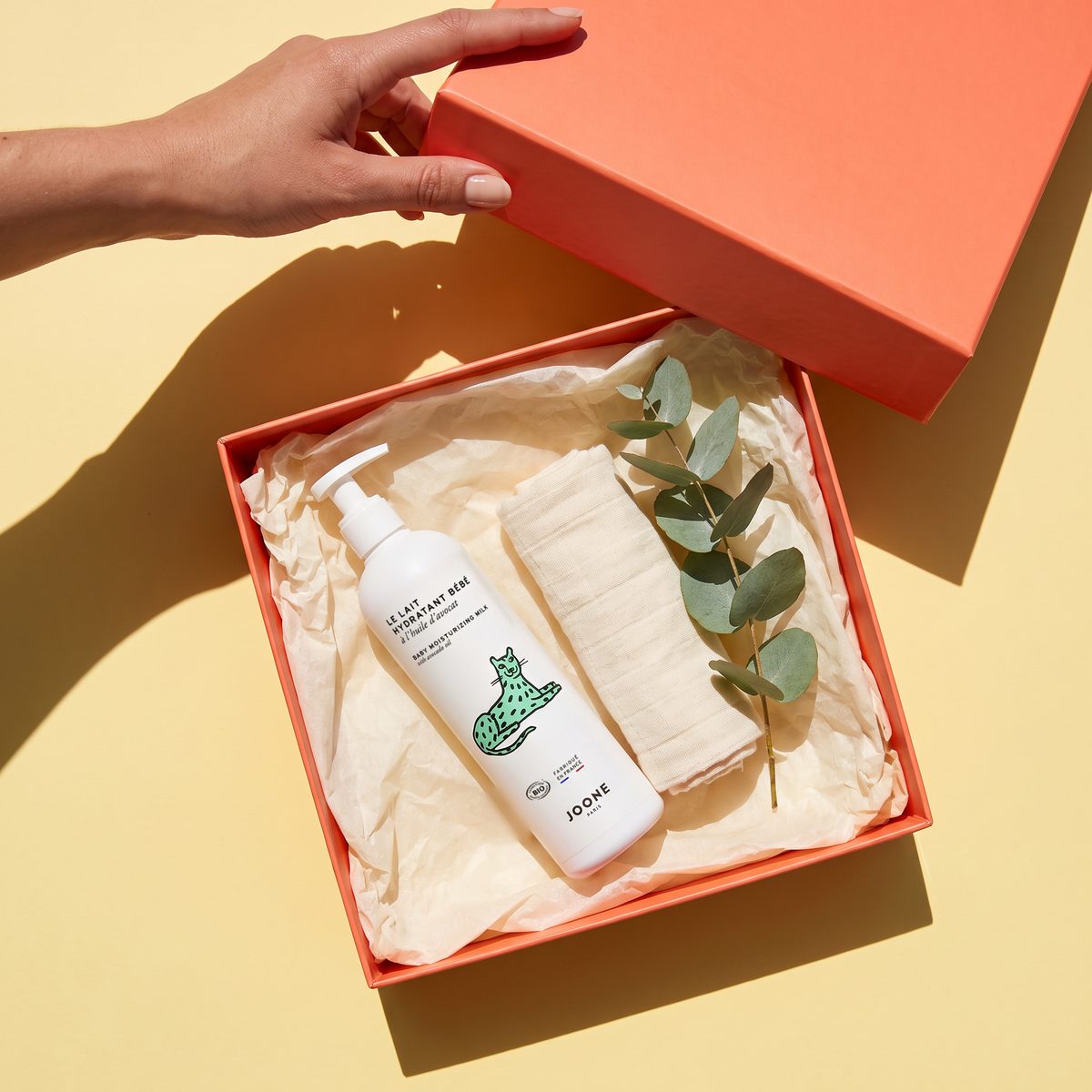 hand tilt het deksel van een koraalrode pr-doos met joone lait hydratant bébé in zijdepapier
